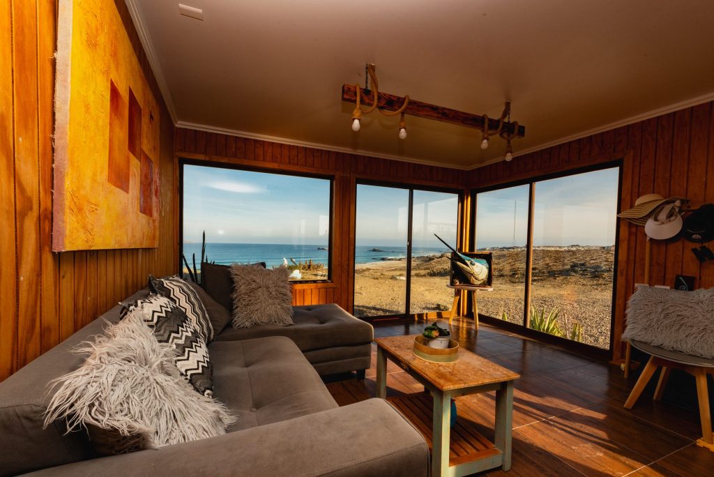 Living de una cabaña del lodge con ventanales hacia el mar